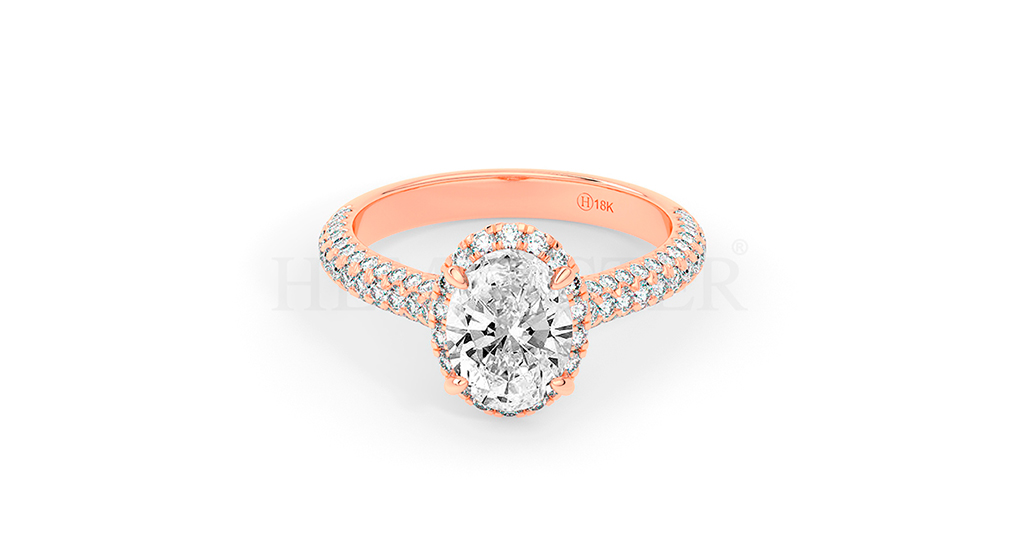 Anillo de compromiso estilo clúster, resalta un hermoso diamante forma brillante oval central y un ruedo de diamantes adicionales en forma de flor.